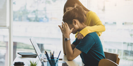 One female colleague comforting a overwhelmed and upset female colleague at her desk