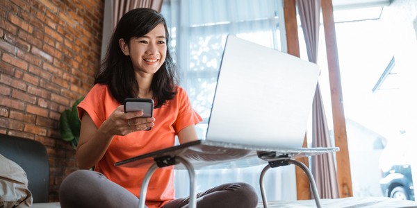 Woman works from her bed on her laptop and phone